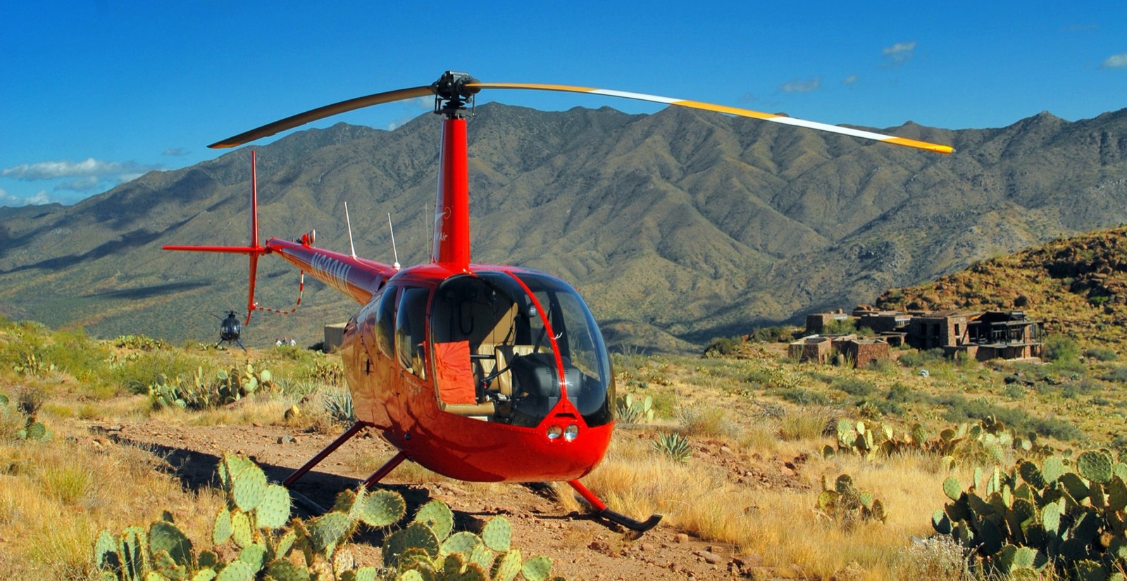 Robinson R44 rouge posé dans un décor montagneux, vue trois-quarts avant