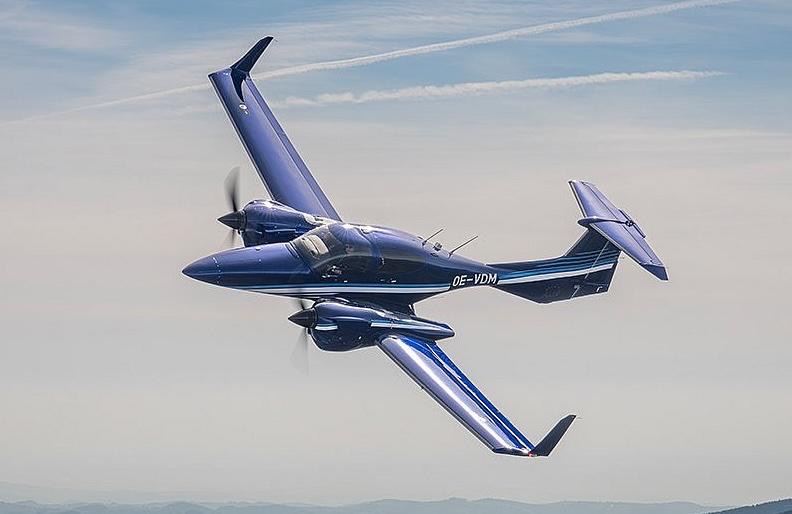 Diamond DA42-VI bleu et blanc en vol, train rentré, vue de trois-quarts arrière