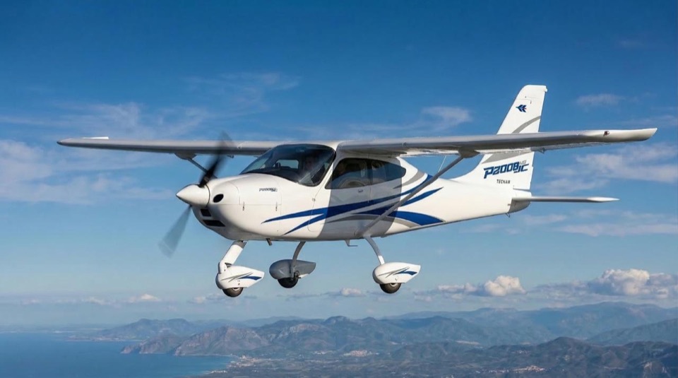 Tecnam P2008 JC NG blanc et bleu en vol au-dessus de la côte